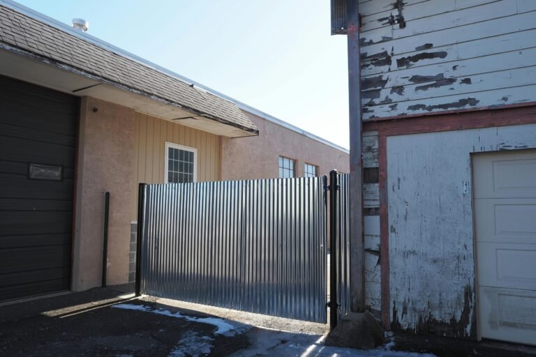 An image depicting rustic buildings with corrugated metal fencing and peeling paint in an industrial area.